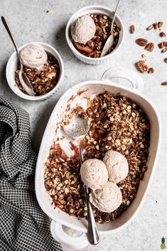 two bowls filled with ice cream and granola on top of a table next to spoons