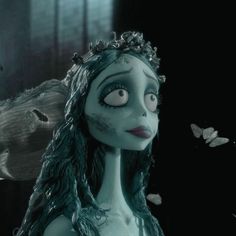 a woman with blue hair and makeup is staring at butterflies in the air above her head