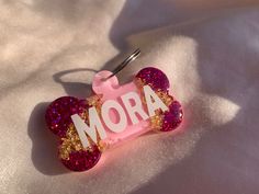 a pink and gold dog bone shaped keychain with the word mora printed on it