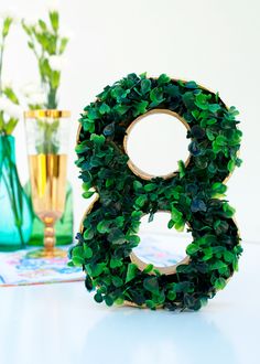 the number eight is made out of green leaves and sits next to vases with flowers