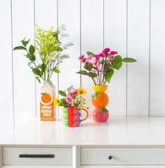 three vases filled with flowers sitting on top of a white table next to drawers