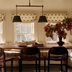 a dining room table with four chairs and a bench in front of two windows that have roman shades on them