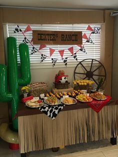 a dessert table is set up in front of a large green cactus and other decorations