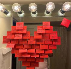 a bunch of red sticky notes attached to a mirror with light bulbs above it that are hanging from the ceiling