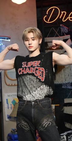 a young man flexing his muscles in front of a store window with neon signs behind him