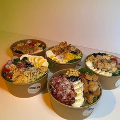 four bowls filled with different types of food on top of a white countertop in front of a yellow wall