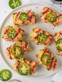 several small sandwiches are arranged on a white plate with green peppers and sauces next to them