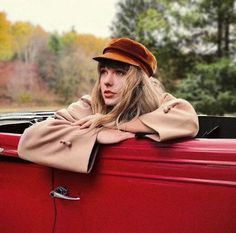 a woman leaning on the hood of an old red car with her arms folded out