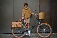 a woman standing next to a bike with a basket on the front and back wheel