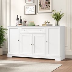 a white sideboard in a living room with pictures on the wall above it and a potted plant next to it