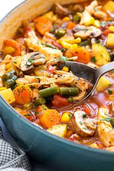 a pot filled with chicken and vegetable stew on top of a blue cloth next to a wooden spoon