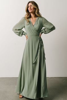 a woman in a long green dress standing with her hands on her hips and looking off to the side