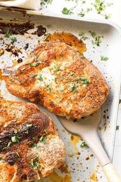 two pork chops sitting on top of a pan with parsley sprinkled on them