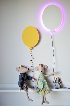 two stuffed mice are sitting on a shelf with a balloon attached to the wall behind them