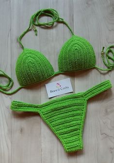 two green bikinisuits are laying on a white wooden floor and one has a name tag attached to it