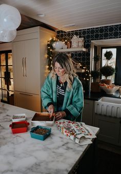 a woman is preparing food on the counter in her kitchen with christmas lights behind her