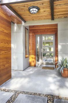 the entrance to a modern home with wood and glass doors, graveled walkway and potted plants on either side