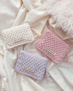 three small crocheted purses sitting on top of a white bed next to a fluffy pillow