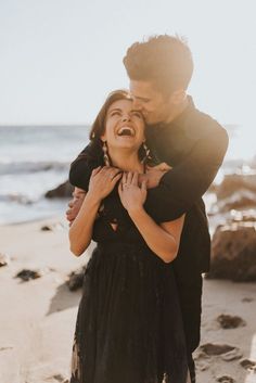 a man and woman are hugging on the beach while one holds his face to her chest