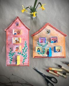 two paper houses sitting on top of a table next to some scissors and flowers in a vase