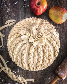 an apple pie sitting on top of a wooden table next to a knife and two apples