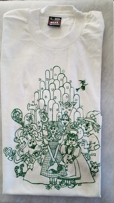 Whimsical Cartoon Art on T-shirt. Emerald Green ink on White Tee. Wicked Witch flies over Emerald City. White 50/50 Best. Select Size.  Adult Sizes. Matching mug with same design. White Band Merch Top With Custom Artwork, Wizard Of Oz Cartoon, Cartoon T Shirt, Wicked Witch, Emerald City, Cartoon T Shirts, Wizard Of Oz, Green Design, White Tee