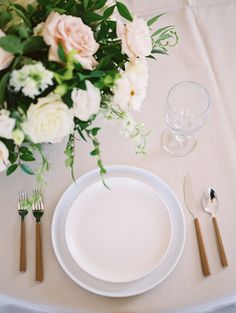 the table is set with white plates, silverware and pink flowers in vases