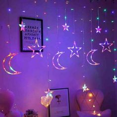 some stars and moon lights hanging from the ceiling above a bed in a room with purple walls