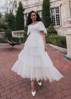 a woman standing in front of a large building wearing a white dress with tiered layers