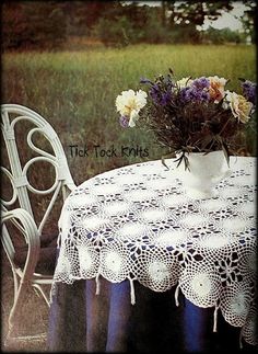 a white table topped with a vase filled with flowers next to a white chair and table cloth