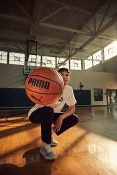 a young man holding a basketball on top of a hard wood floor in an indoor gym