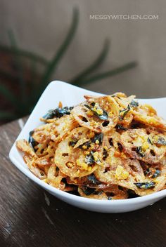 a white bowl filled with fried food on top of a wooden table next to a plant