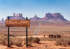 a wooden sign in the desert with mountains in the background