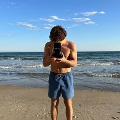 a man standing on top of a beach next to the ocean holding a cell phone