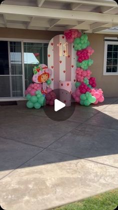 the balloon arch is decorated with pink, green and white balloons in front of a house