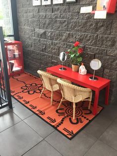 a red table with two chairs and a potted plant on top of it in front of a brick wall