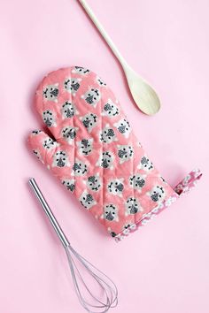 a pink oven mitt next to a whisk and utensil on a pink background