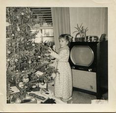 an old black and white photo of a woman decorating a christmas tree