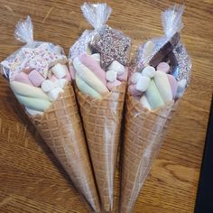 three cones filled with marshmallows and candies on top of a wooden table