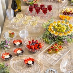 the table is covered with many plates and bowls of fruit, wine glasses, and flowers