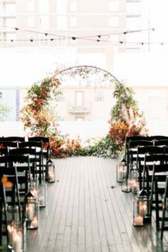 rows of chairs with candles in them on a wooden floor next to an arch decorated with flowers and greenery