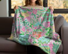 a woman holding up a pink and green floral print blanket in front of a window