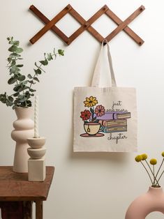 a tote bag hanging on a wall with flowers and books next to vases