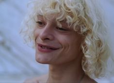 a close up of a person with blonde hair and a necklace smiling at the camera