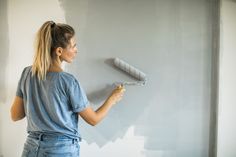 a woman is painting the wall with white paint and she has a roller in her hand