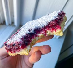 a hand holding a piece of cake with blueberries and powdered sugar on it