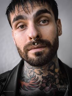 a man with tattoos and piercings on his face looks at the camera while wearing a leather jacket