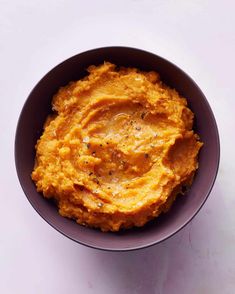 a bowl filled with mashed sweet potatoes on top of a white countertop next to a spoon