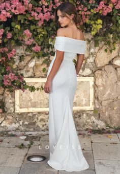 a woman wearing a white dress standing in front of a stone wall with pink flowers