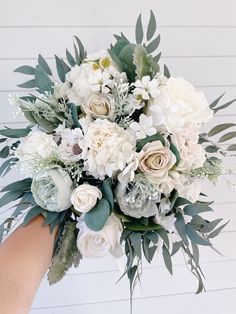 a bouquet of white flowers and greenery is being held by someone's hand